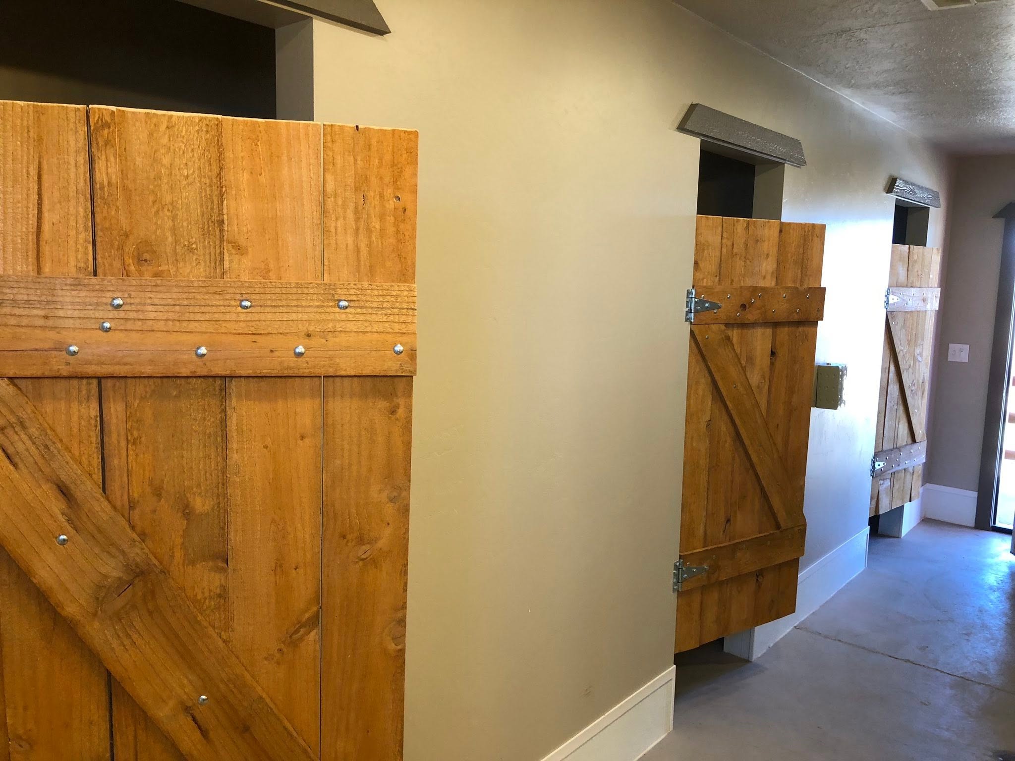 Wooden stall doors along a clean, brightly lit corridor at the equestrian facility.