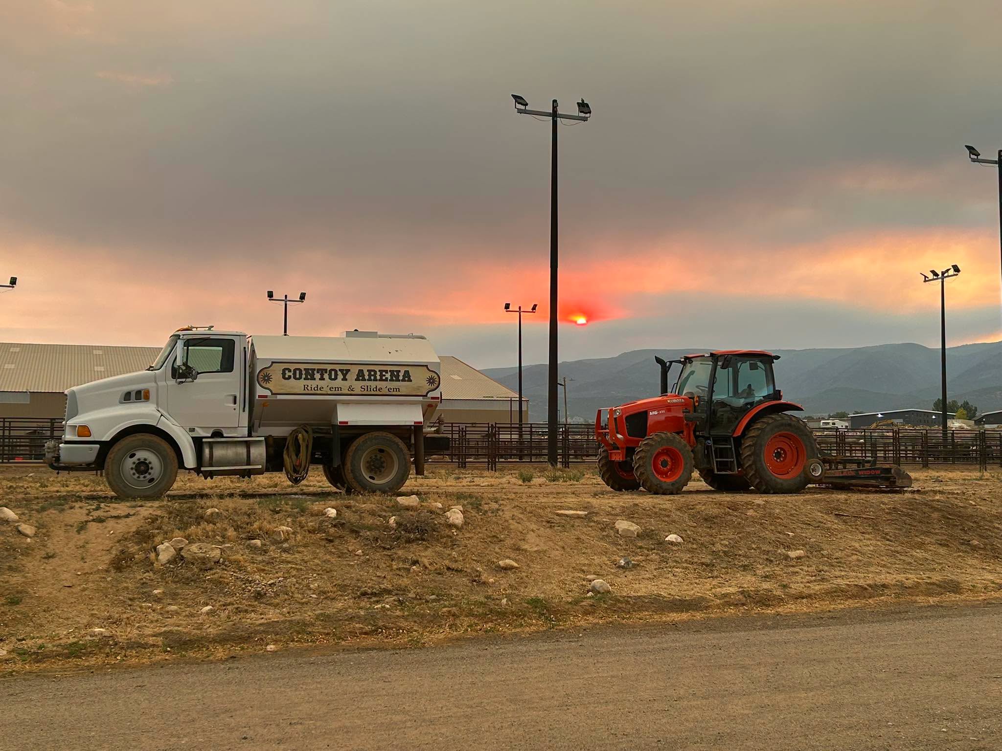 Contoy Arena water truck and orange tractor parked outdoors at sunset.